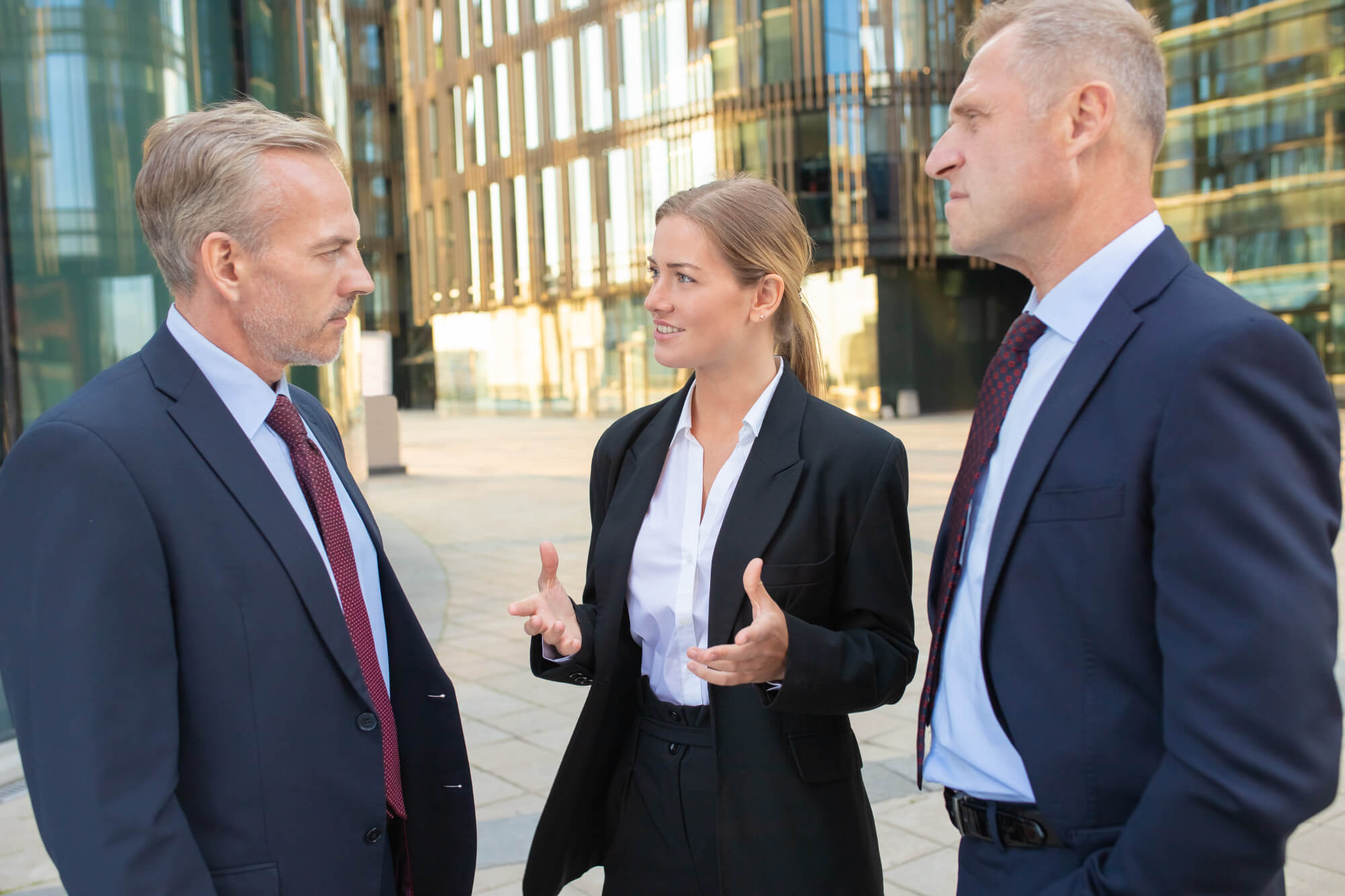 Three business professionals engaged in conversation outside a modern office building.