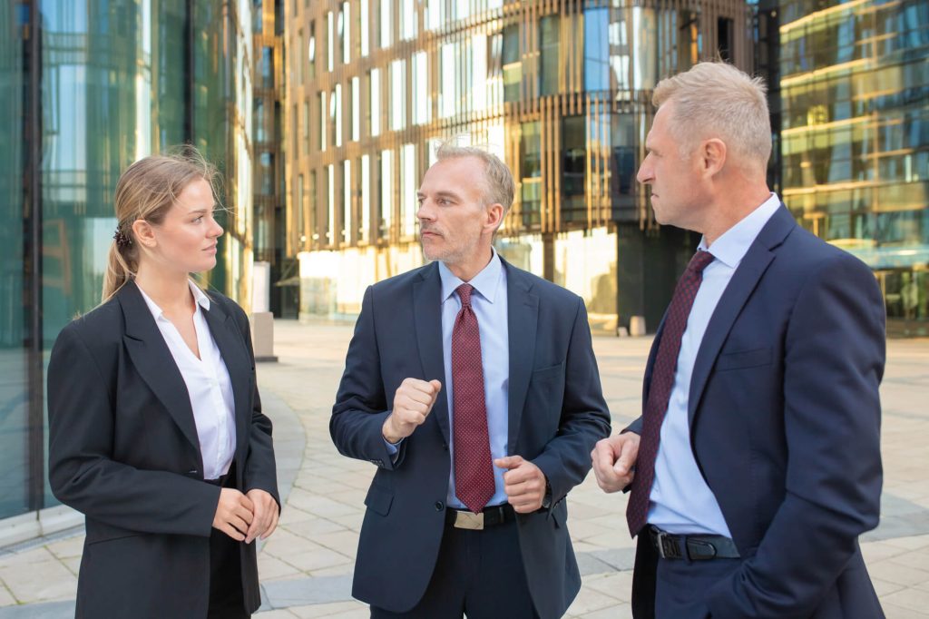 Three business professionals engaged in conversation outside a modern office building.
