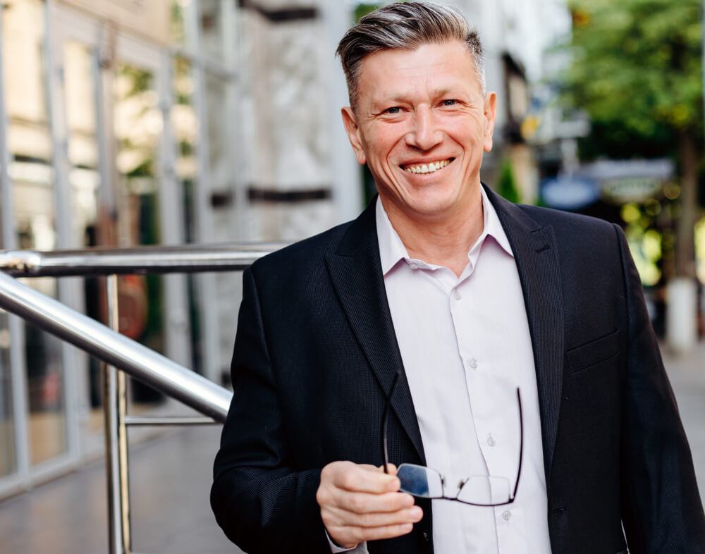 happy senior businessman holding glasses in his hand in city